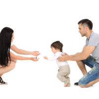 Cute smiling baby girl learning to walk with parents