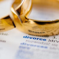 Two broken wedding rings on divorce word in dictionary.