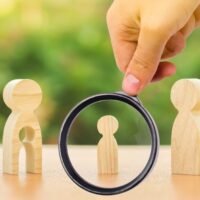 A magnifying glass looks at a child’s figure stands between father and mother. The child chooses which parent to live with after their divorce. Guardianship over child. interest of child