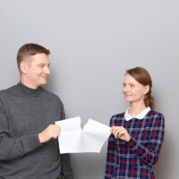 Studio shot of adult couple holding and tearing paper sheet