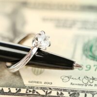 Wedding ring on pen, on banknotes background. Marriage of convenience