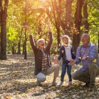 Grandparents and grandchild throwing leaves in park and having fun together