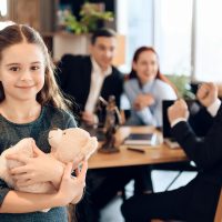 Happy little girl is hugging teddy bear at office of family lawyer. Registration of guardianship. Family in office of family lawyer.