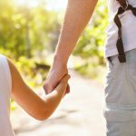 child holding hand of adult parent outside in summer park