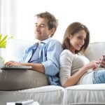 Young couple relaxing on sofa with digital tablet and laptop.