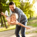 Carefree summer moment. Excited father holding his cute daughter on hands, playful girl enjoying freedom of flying, family enjoy moment of happiness in park