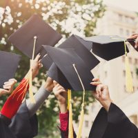 A group of multietnic students celebrating their graduation by throwing caps in the air closeup. Education, qualification and gown concept.