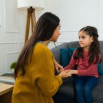 Concerned loving mother talking to her young daughter about divorce and child custody while sitting on the sofa