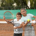 Happy children with tennis racket and ball on court outdoors