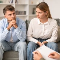 Young couple having therapy session to navigate marital issues, sitting on the sofa in psychotherapist's office, spouses solving relationship conflicts with professional. Selective focus