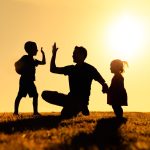 Father interacting playing outdoors with his children giving high five. Parenting and fatherhood concept.