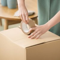 Woman's hand putting duct tape on cardboard boxes when packing for a move Faceless