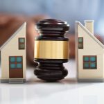 Close-up Of A Judge Striking Gavel Between Split House Over Reflective Desk