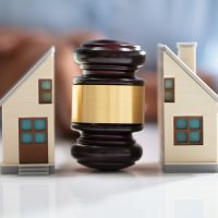 Close-up Of A Judge Striking Gavel Between Split House Over Reflective Desk