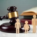 Legal dispute photo shows wooden figures representing family. Couple, child stand near gavel, books. Concept of divorce custody. Family facing court decision. Problem of separation. Legal