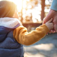 Close up of mother and a child hands at the sunset. A parent holds the hand of a small boy in the sunset. Mother holding her little boys hand walking down the street Close up of mother and a child hands at the sunset. A parent holds the hand of a small boy in the sunset. Mother holding her little boys hand walking down the street