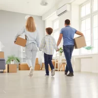 Backside view of an parents and son celebrate relocation to a new home, holding moving boxes in a display of family togetherness. New property ownership, real estate, and shared wealth.