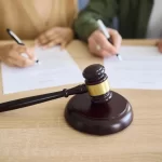 A couple signing divorce documents at court with a gavel in the foreground, representing legal family proceedings